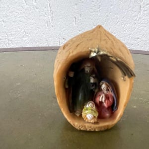 Può includere: Un piccolo presepe in ceramica marrone all'interno di un guscio di noce scavato. Le figure sono di Maria, Giuseppe e Gesù bambino.