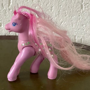 May include: A pink pony toy with a long pink mane and tail. The pony has a floral pattern on its body and blue eyes.