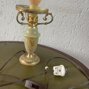 Op de afbeelding: Een gouden tafellamp met een albasten voet en een witte bol. De lamp heeft een snoer met een schakelaar en een stekker.
