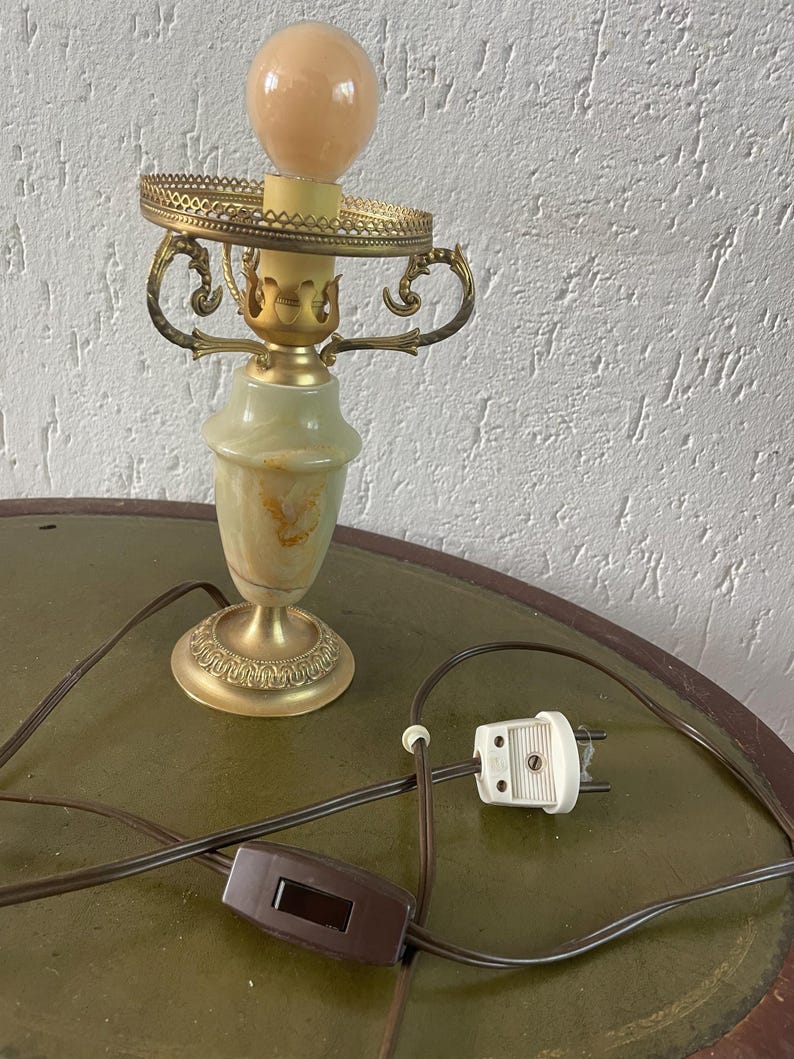 Op de afbeelding: Een gouden tafellamp met een albasten voet en een witte bol. De lamp heeft een snoer met een schakelaar en een stekker.