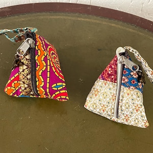 May include: Two small triangular fabric pouches with zipper closures. One pouch is pink, orange, and blue with a brown zipper. The other pouch is white, gold, and blue with a silver zipper.