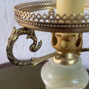 Op de afbeelding: Een vintage albasten tafellamp met een gouden metalen voet en sierlijke details. De lamp heeft een ronde, opengewerkte kaphouder en een decoratieve handgreep.