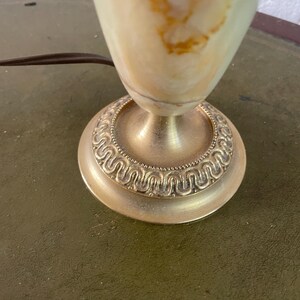 Op de afbeelding: Een witte alabaster tafellamp met gouden accenten. De lampvoet heeft een decoratief, versierd ontwerp.