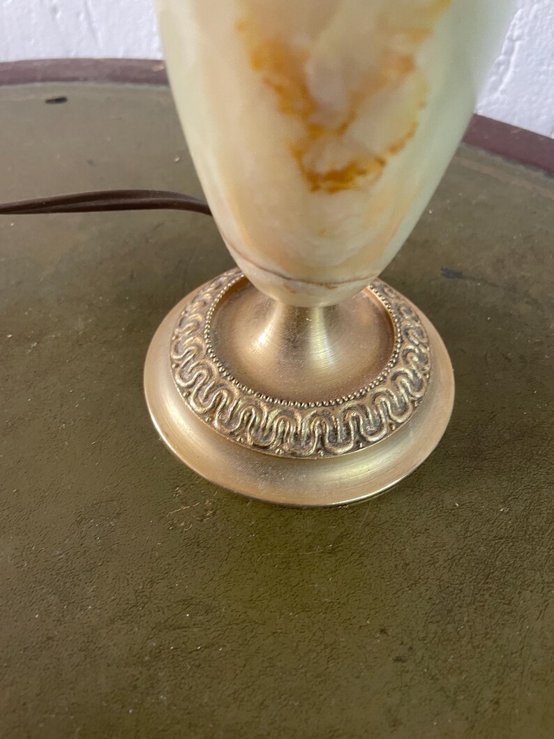 Op de afbeelding: Een witte alabaster tafellamp met gouden accenten. De lampvoet heeft een decoratief, versierd ontwerp.