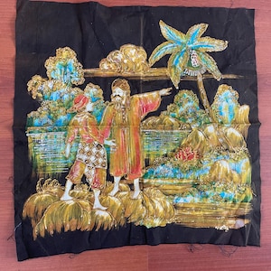 May include: A black fabric wall hanging with a gold, blue, and red painted scene of two figures standing in a landscape with palm trees.