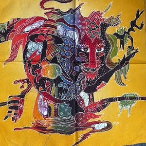 Op de afbeelding: Een kleurrijk batiktextiel met een levendig, abstract ontwerp. Het kunstwerk toont een centrale gezichtachtige figuur met rode, paarse en zwarte elementen, omringd door ingewikkelde patronen in verschillende kleuren. De achtergrond is warm geel.