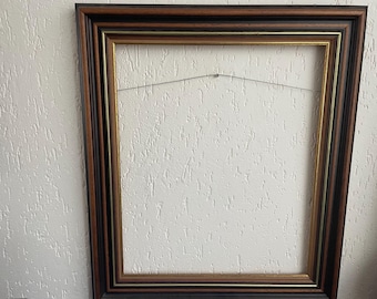 May include: A rectangular picture frame with a dark brown and black border, with a thin gold inner edge. A wire is strung across the back for hanging. The frame is empty, ready for a photograph or artwork.