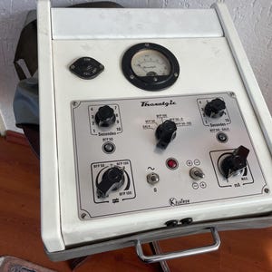Puede incluir: Un dispositivo médico blanco con perillas y diales negros. El dispositivo tiene una etiqueta que dice "Thoralogie" y "Klatron".