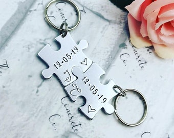May include: Silver puzzle piece keychain with the date 12.05.19 engraved on each piece. The pieces fit together to form a heart.