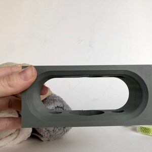 May include: Gray 3D printed toothbrush holder with four slots and a large oval opening. The holder is made of a smooth, matte material.