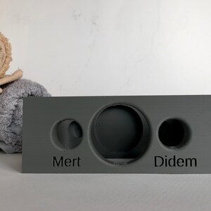 May include: A gray rectangular block with three circular cutouts. The block has the names "Mert" and "Didem" inscribed on the front.