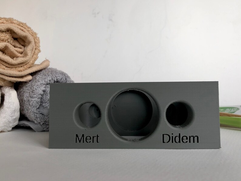 May include: A gray rectangular block with three circular cutouts. The block has the names "Mert" and "Didem" inscribed on the front.