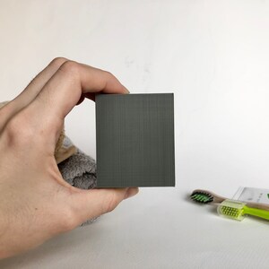 May include: A dark gray rectangular bar of soap.