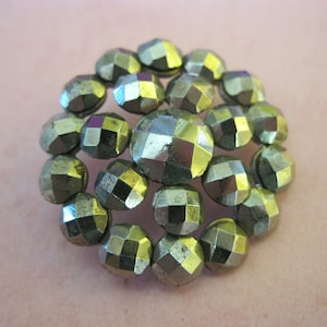 May include: A vintage brooch with a circular design. The brooch features numerous faceted, metallic-coloured beads arranged in a cluster. The beads have a dull, aged appearance, suggesting they are antique or vintage.