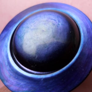 May include: A circular, blue decorative item with a dark central area and a ringed, iridescent outer edge. The object has a glossy finish and seems to be made of glass or a similar material. The colour shifts from dark blue to lighter shades.