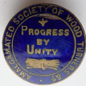 May include: A blue and gold enamel badge with the text "Amalgamated Society of Wood Turners" around the edge. In the centre is a gold dove with the text "Progress by Unity" and a stylised image of a bundle of wood.