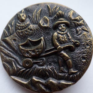 Antique metal picture button - man pulling cart watched by rabbit - black japanned base & loop shank 1.1/4"