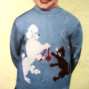 May include: A light blue knitted jumper with a white poodle and a brown cat playing with a red toy. The jumper has a ribbed collar and cuffs. The design is a playful, vintage style.