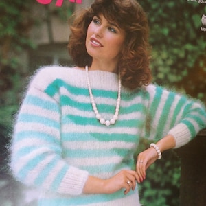 May include: A white and turquoise striped sweater with a fuzzy texture. The sweater has a round neckline and long sleeves. The model is wearing a white pearl necklace and a white bracelet.