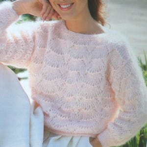 May include: A pale pink, long-sleeved jumper with a detailed, openwork design. The jumper has a round neck and a soft, fluffy texture. The sleeves are long, and the overall style is feminine and comfortable.