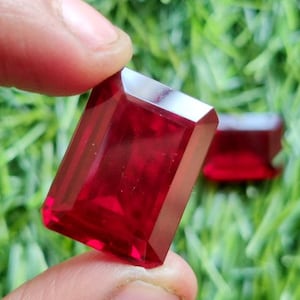 Puede incluir: Dos piedras preciosas rectangulares de color rojo intenso con corte facetado.