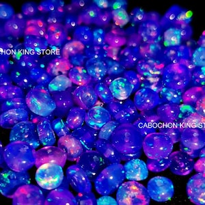May include: A close-up shot of a collection of iridescent, oval-shaped gemstones. The stones are primarily deep blue and purple, with flashes of pink, green, and blue. The text "CABOCHON KING STORE" is visible.