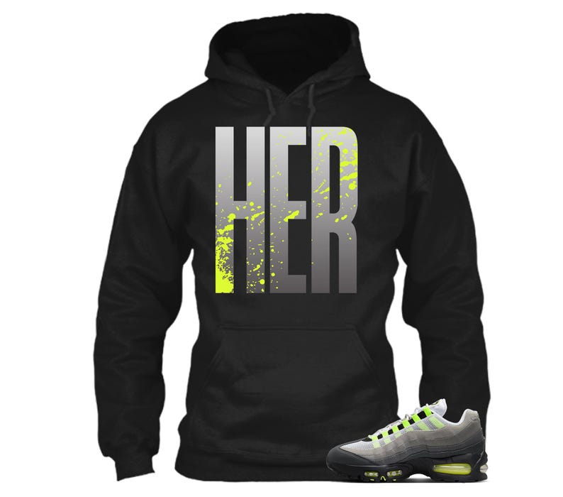 Puede incluir: Sudadera con capucha negra con la palabra "HER" en letras grises grandes con salpicaduras de color amarillo ne&oacute;n. Un par de zapatillas deportivas grises, negras y amarillo ne&oacute;n en primer plano.