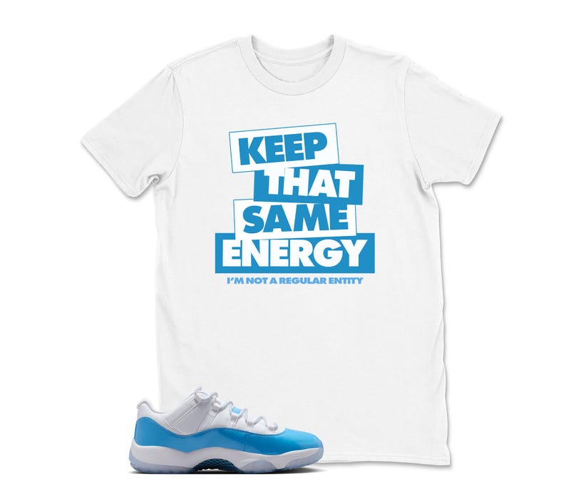 May include: White t-shirt with the text "KEEP THAT SAME ENERGY" in blue block letters. Below the text is the phrase "I'M NOT A REGULAR ENTITY". A pair of blue and white sneakers is in the foreground.
