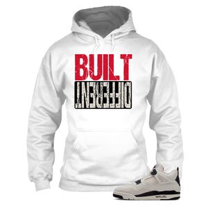 May include: White hoodie with the text "BUILT DIFFERENT" in red and black. The hoodie has a front pocket and a gray-lined hood. A pair of white, black, and red sneakers are in the image.