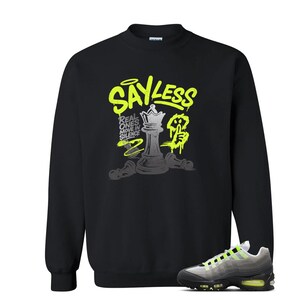 Puede incluir: Sudadera negra con un dise&ntilde;o gr&aacute;fico en verde ne&oacute;n y gris. El gr&aacute;fico incluye el texto "SAY LESS" y una pieza de ajedrez. Un par de zapatillas grises y negras con detalles en verde ne&oacute;n est&aacute;n en la esquina inferior derecha.