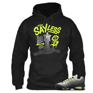 Puede incluir: Sudadera con capucha negra con el texto "SAYLESS" en verde ne&oacute;n y un dise&ntilde;o de pieza de ajedrez. Un par de zapatillas grises y negras con detalles en verde ne&oacute;n en primer plano.