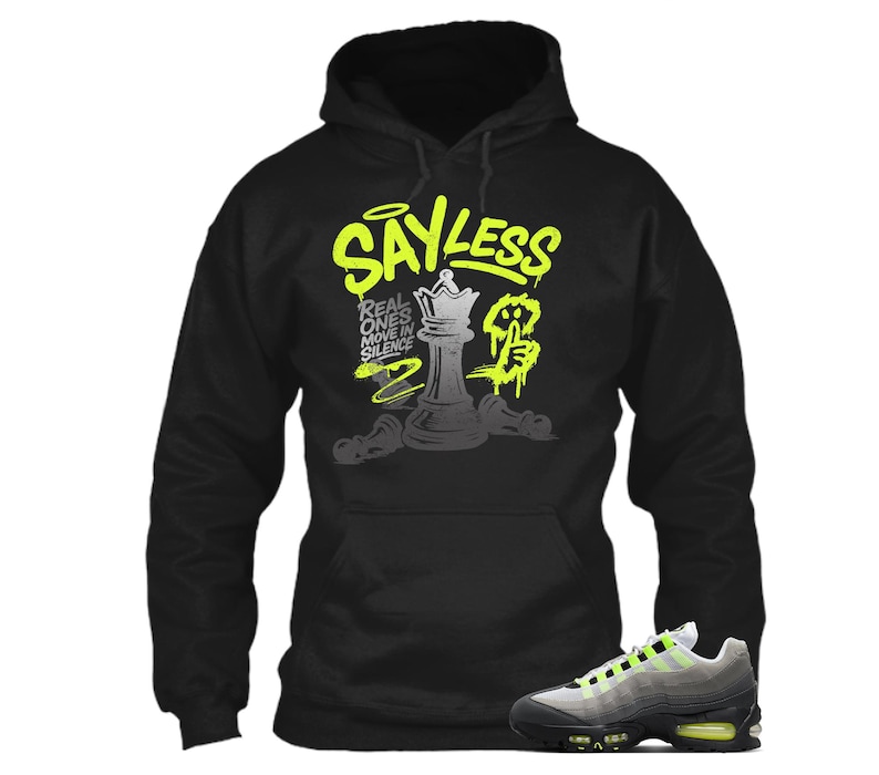 Puede incluir: Sudadera con capucha negra con el texto "SAYLESS" en verde ne&oacute;n y un dise&ntilde;o de pieza de ajedrez. Un par de zapatillas grises y negras con detalles en verde ne&oacute;n en primer plano.