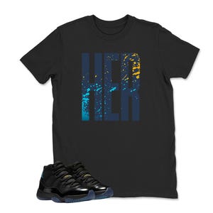 Op de afbeelding: Zwart T-shirt met het woord "HER" in een blauw en geel spatterontwerp. Een paar zwarte en blauwe sneakers staan onderaan de afbeelding.