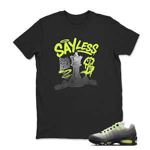 Puede incluir: Camiseta negra con un gr&aacute;fico verde ne&oacute;n y gris. El gr&aacute;fico incluye las palabras "SAY LESS" y una pieza de ajedrez. Una zapatilla deportiva gris y verde ne&oacute;n est&aacute; en la esquina inferior derecha.
