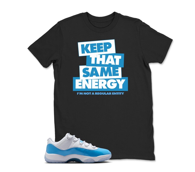 May include: Black t-shirt with the text "KEEP THAT SAME ENERGY" in white and blue. Below the text is "I'M NOT A REGULAR ENTITY". A pair of white and blue sneakers is in the foreground.