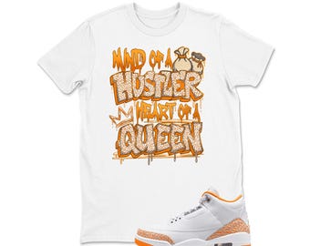 May include: White t-shirt with orange text that reads "Mind of a Hustler Heart of a Queen" and a pair of money bags. A white and orange sneaker is in the foreground.