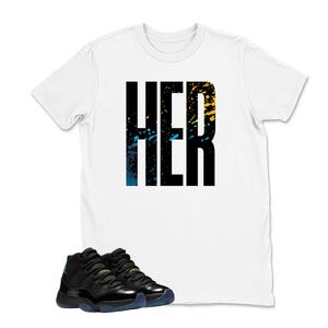 Op de afbeelding: Een wit t-shirt met het woord "HER" in grote zwarte blokletters, geaccentueerd met blauwe en gele verfspatten. Daaronder een paar zwarte en teal sneakers.