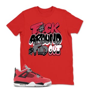May include: Red t-shirt with the text "F#ck Around & Find Out" in a graffiti-style design. A pair of red and black sneakers with white and gray accents are in the foreground.