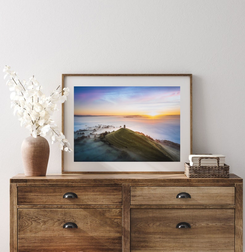May include: A framed photograph of a hilltop with a stone tower at the summit, surrounded by fog and a colorful sunrise in the distance.