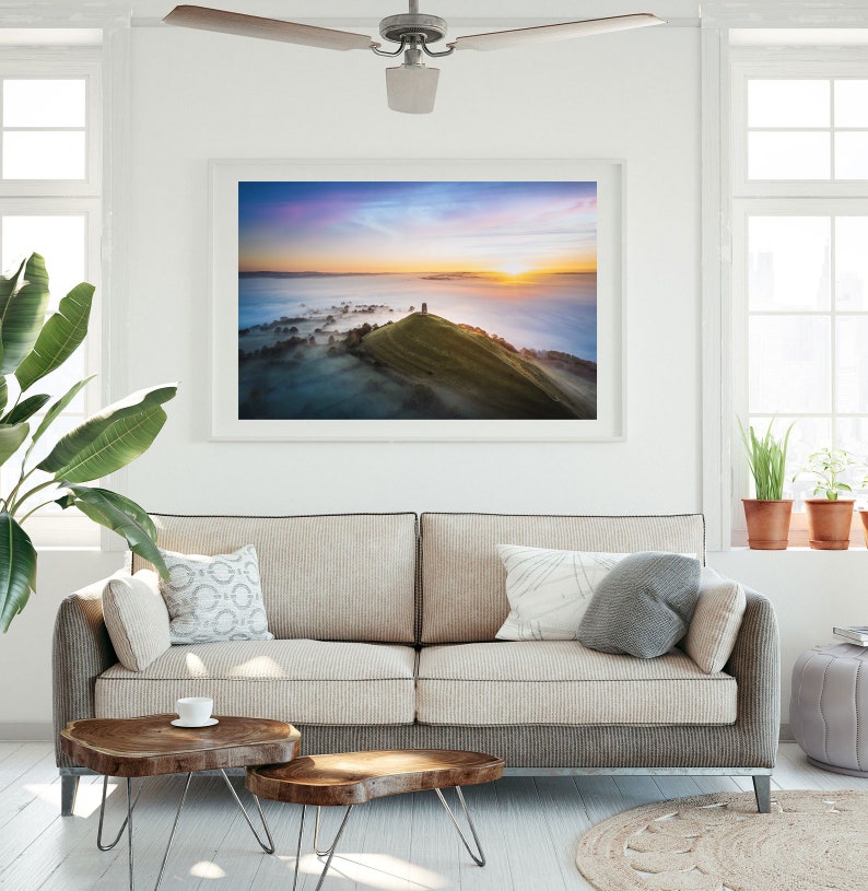 May include: A framed photograph of a hilltop with a tower at the peak, surrounded by fog and a colorful sunrise in the background.
