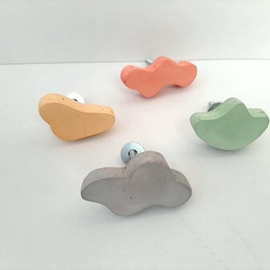 以下が含まれることがあります： 異なる色（薄いオレンジ、薄い黄色、薄い緑、薄い灰色）の抽象的な雲の形をしたキャビネットノブが4つあります。