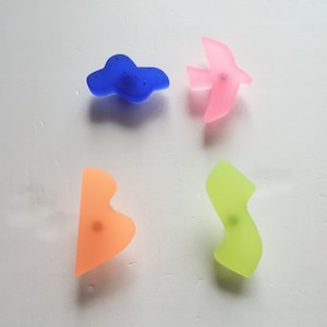 Op de afbeelding: Vier kleurrijke wandhaken in de vorm van een wolk, een vogel, een kriebel en een gebogen vorm. De haken zijn gemaakt van doorschijnend plastic en hebben een matte afwerking.