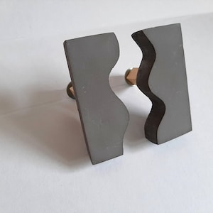 May include: Two gray ceramic bookends shaped like wavy lines. The bookends are standing on a white surface.