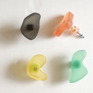 Peut inclure: Quatre crochets muraux de forme abstraite en différentes couleurs. Les crochets sont en plastique translucide et ont une vis métallique à l'arrière. Les couleurs sont gris, pêche, jaune et vert.