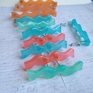 Peut inclure: Un ensemble de 10 boutons de cabinet ondulés dans différentes nuances de bleu, vert et rose. Les boutons sont en résine et ont une finition brillante.