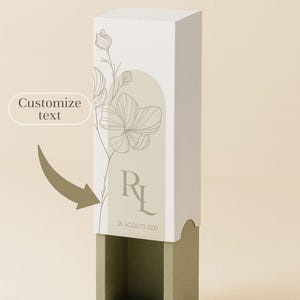 Può includere: Una scatola regalo rettangolare e alta, con una sezione superiore bianca e una base verde salvia. La scatola presenta un motivo floreale e le iniziali "RL" con la data "26 AGOSTO 2025". Le parole "Customize text" sono anch'esse visibili.