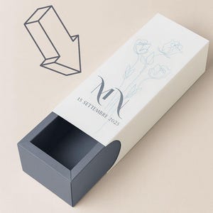 Op de afbeelding: Een witte rechthoekige doos met een grijze schuiflade. De doos is versierd met een bloemenontwerp en de initialen "MN" met de datum "15 Settembre 2025". De tekst "Customize Text" staat bovenaan.