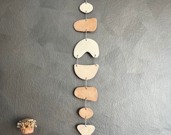 May include: A beige and brown ceramic mobile with geometric shapes hanging from a string. The mobile is made of seven pieces, each with a different shape and size. The mobile is hanging against a gray background.