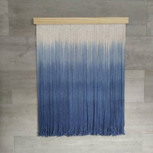 Può includere: Un arazzo da parete in filato blu e bianco ombré con un listello di legno in alto.
