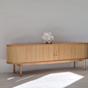 May include: A light wood cabinet with two doors and a geometric white sculpture on top. The cabinet has a rounded top and sits on four legs.
